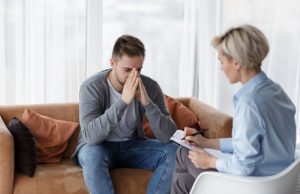 Man in therapy talking about his meth addiction to a professional counselor. His palms are pressed together and he is resting his face in his hands.